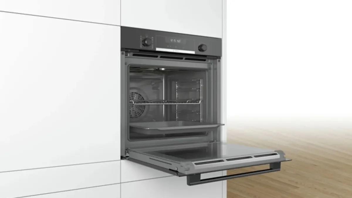 Ein eingebauter, grauer Ofen mit offener Tür ist in einem weißen Schrank mit Holzboden integriert. Im Ofeninneren befinden sich ein Rost und ein Backblech.
