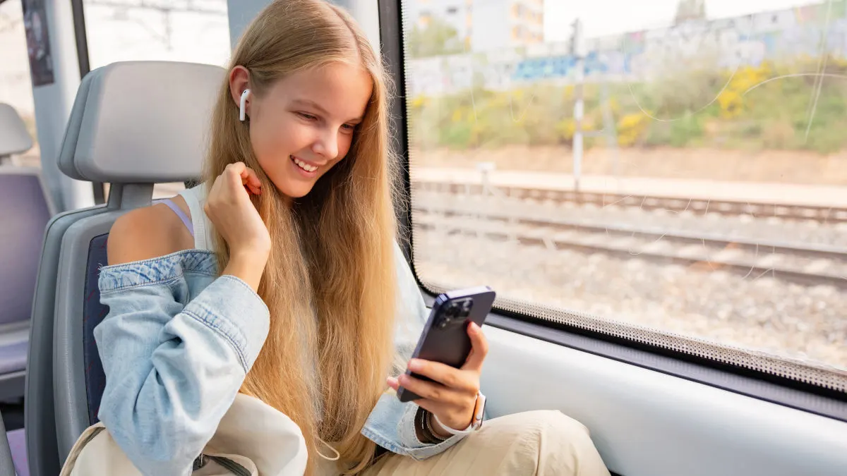 Junge Frau in einem Zug bedient ihr Smartphone.