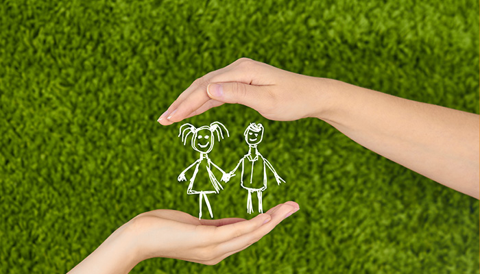 Zwei Hände schützen eine Zeichnung von zwei Kindern, die sich vor einem grünen, grasähnlichen Hintergrund an den Händen halten.