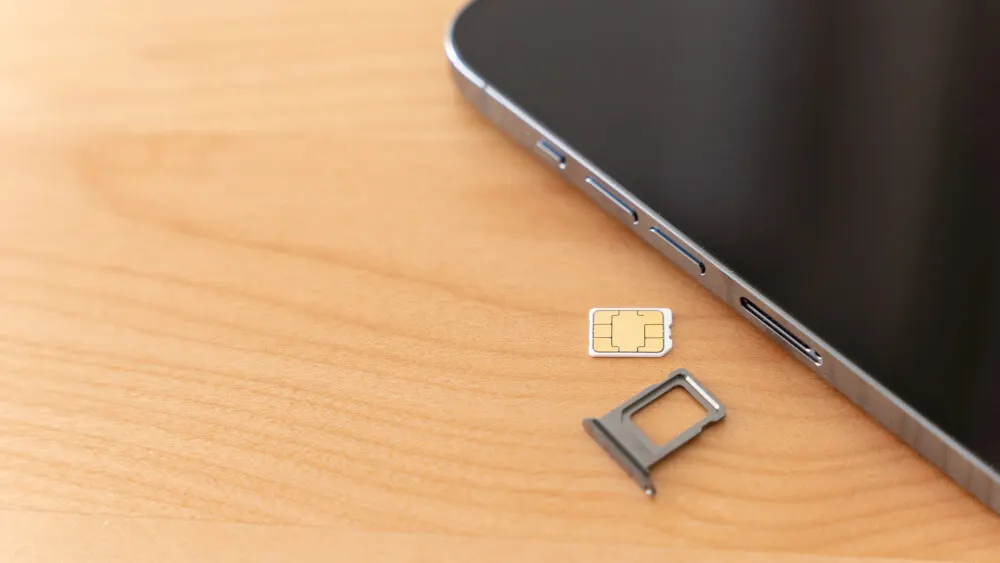 Auf einem Holztisch liegen ein Smartphone, eine SIM-Karte und ein SIM-Karten-Schlitten.