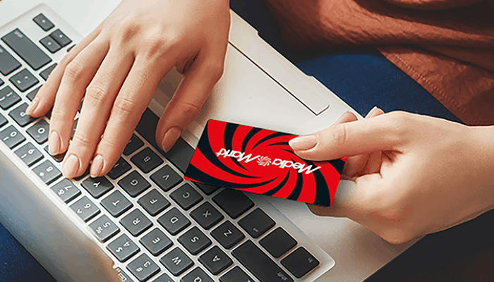 Person tippt auf Laptop-Tastatur, während sie ein rotes MediaMarkt-Preisschild in der anderen Hand hält – Online-Shopping bei MediaMarkt.