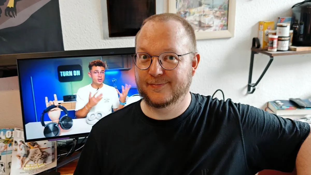 Andreas sitzt vor einem OLED-Monitor, auf dem der TURN ON YouTube-Channel mit Moderator Ilias zu sehen ist.