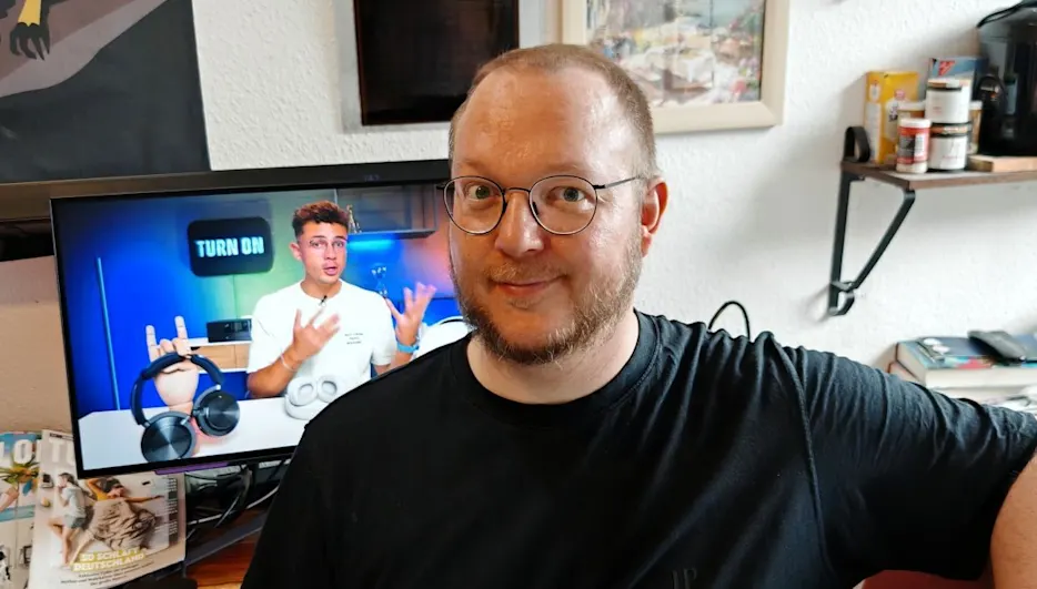 Andreas sitzt vor einem OLED-Monitor, auf dem der TURN ON YouTube-Channel mit Moderator Ilias zu sehen ist.