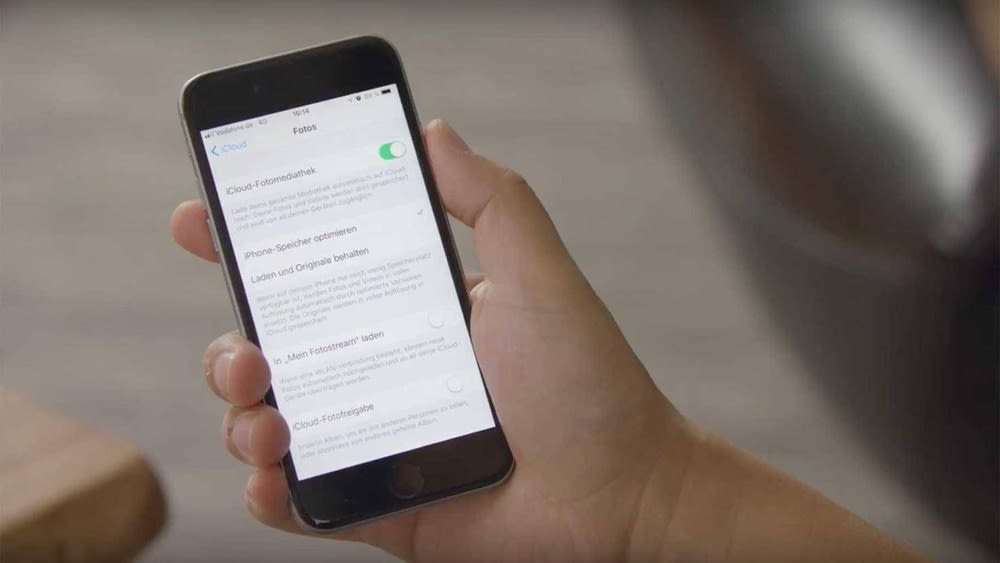 Ein Nutzer hält ein iPhone mit der geöffneten iCloud-Fotomediathek in der Hand.