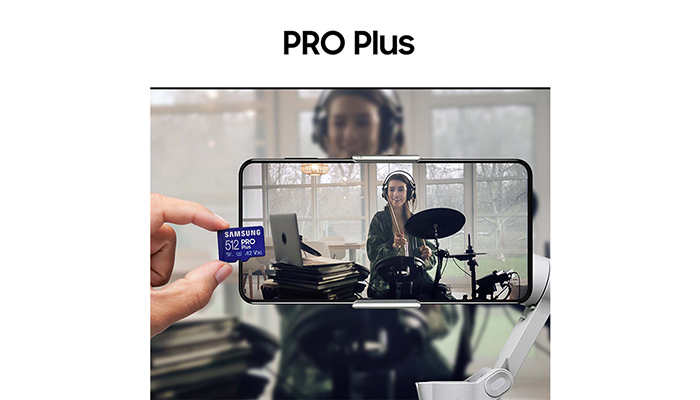 Eine Hand hält eine blaue 512 GB Samsung Speicherkarte vor einem Smartphone, das eine Schlagzeugerin zeigt. Im Hintergrund ist eine Person mit Kopfhörern zu sehen.
