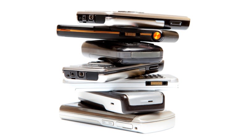 Sieben alte Handys liegen zu einem Stapel aufgetürmt übereinander.