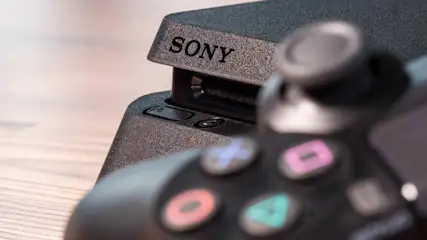 Nahaufnahme einer schwarzen Sony-Spielkonsole mit einem Controller im Vordergrund. Das Sony-Logo ist gut sichtbar.