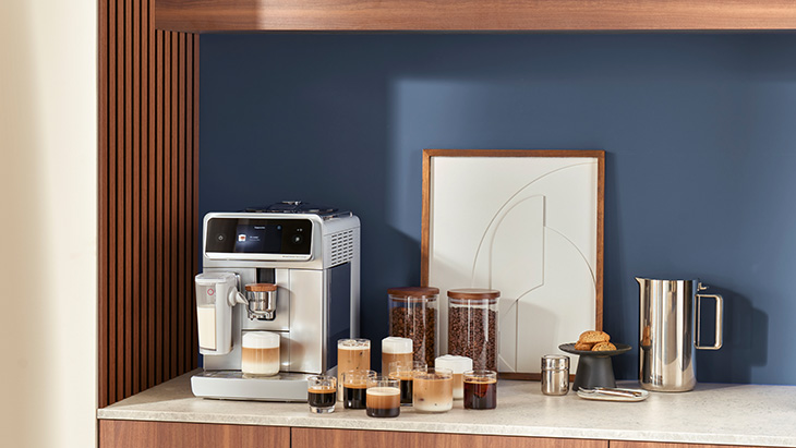 Eine Kaffeemaschine steht in einer Küche, daneben verschiedene Gläser gefüllt mit unterschiedlichen Kaffeespezialitäten.