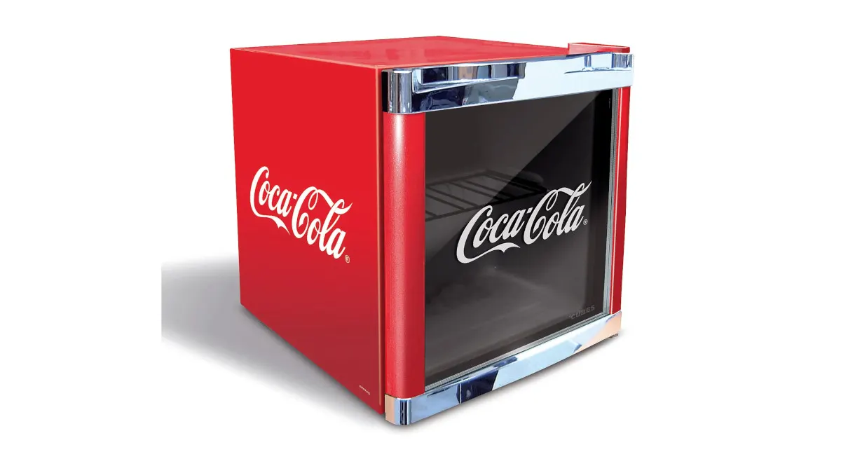 Ein roter, würfelförmiger Coca-Cola-Kühlschrank mit Chromakzenten und Glasfront steht auf einem weißen Hintergrund.