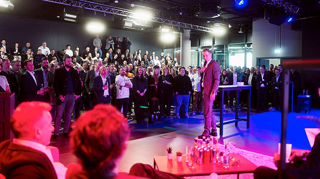 Ein Mann im Anzug hält vor einer großen Menschenmenge eine Rede, stehend auf einem Stapel Dosen. Tische stehen im Vordergrund.