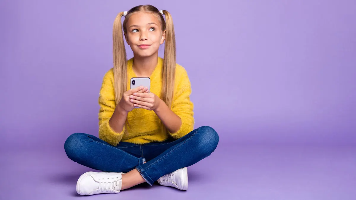 Ein junges Mädchen hält ein Smartphone in den Händen und schaut nachdenklich in die Luft.