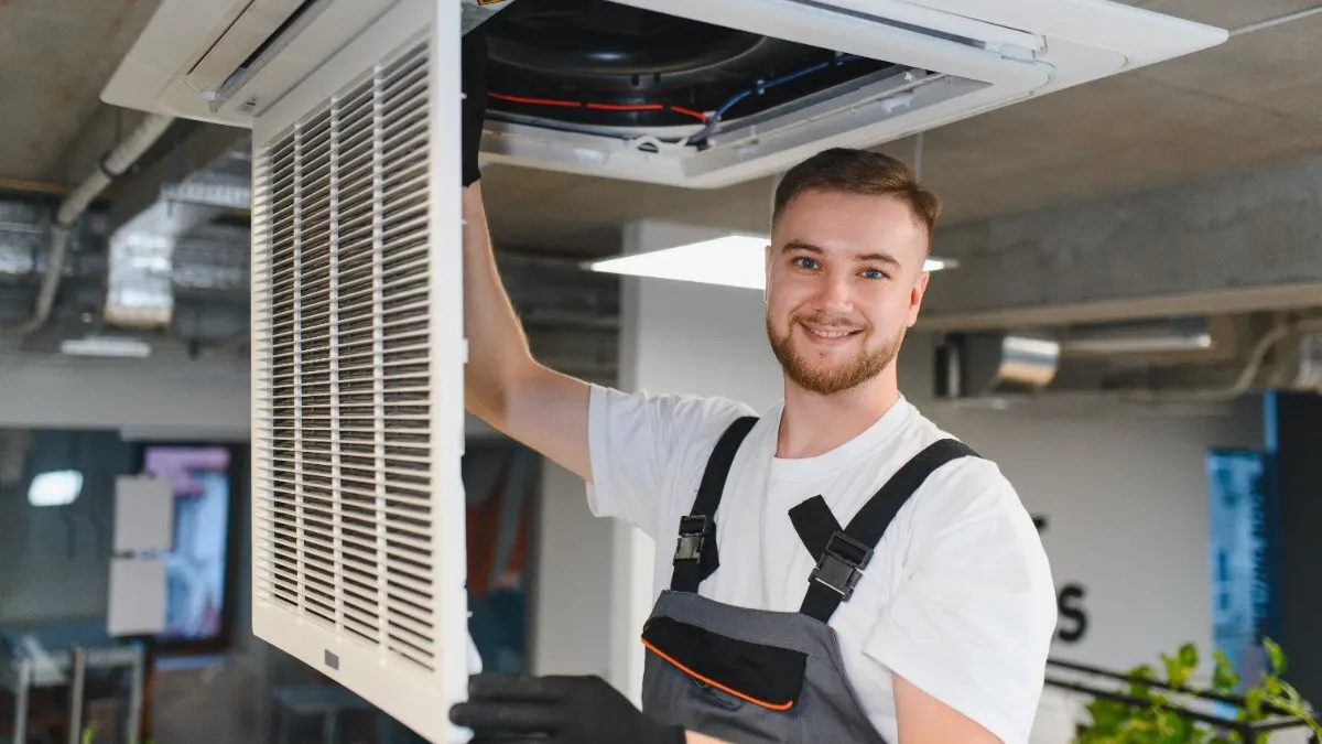 Ein Mann in Arbeitskleidung arbeitet am offenen Deckenauslass einer Klimaanlage.