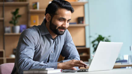 Ein Mann sitzt an einem Schreibtisch und tippt auf einem Laptop.