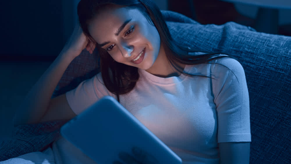 Eine Frau liest auf einer Couch im Dunkeln ein E-Book.