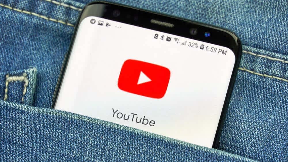 Die YouTube-App ist auf einem Smartphone geöffnet, das in einer Hosentasche steckt.