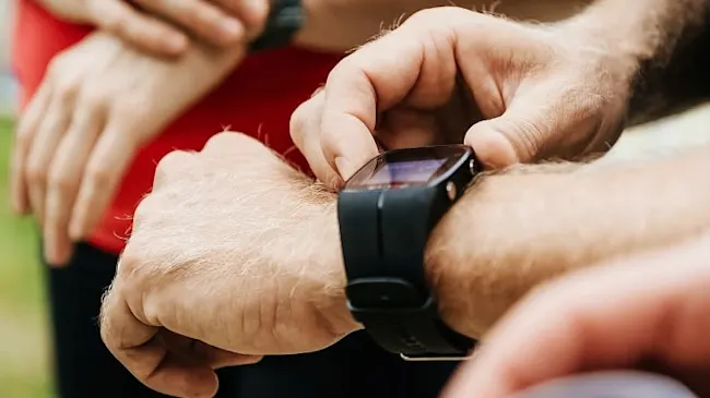 Eine Person justiert eine schwarze Smartwatch am Handgelenk, während andere Personen im Hintergrund stehen.