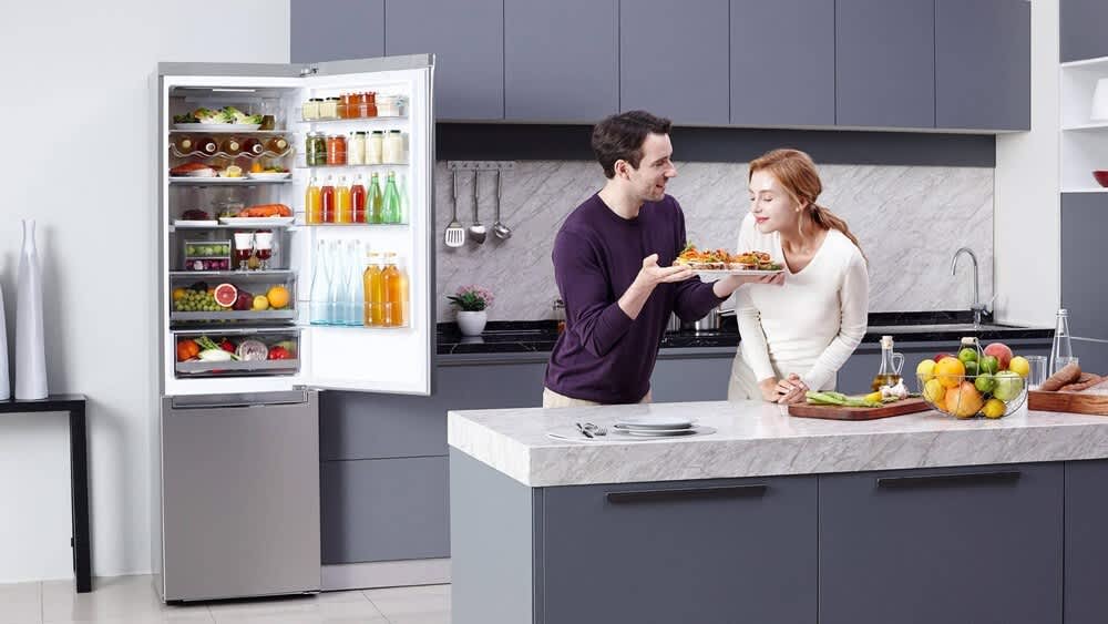Zwei Personen stehen in einer Küche neben einem offenen Kühlschrank.