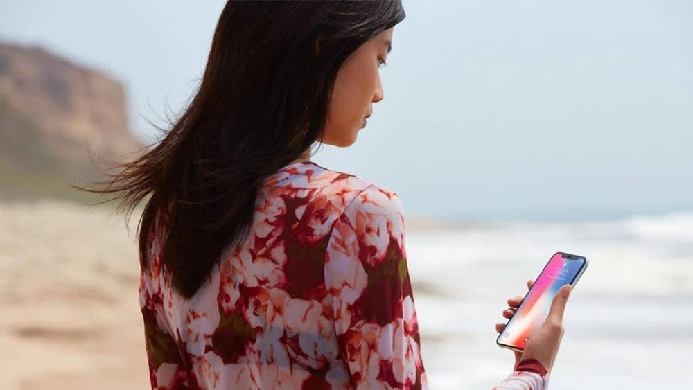 Eine Frau steht am Strand und hält ein iPhone 10 in der Hand.