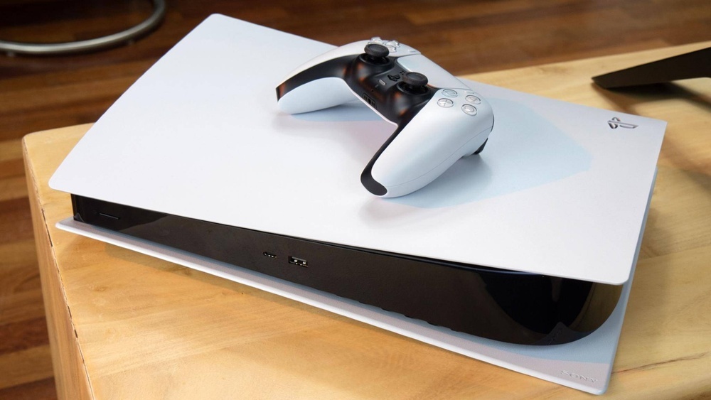 Ein weißer und schwarzer Spielkonsolen-Controller liegt oben auf einer weißen Spielkonsole auf einem Holztisch.