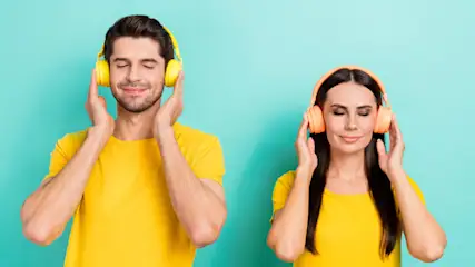 Ein Mann und eine Frau mit gelben Kopfhörern und gelben T-Shirts vor einem türkisfarbenen Hintergrund.
