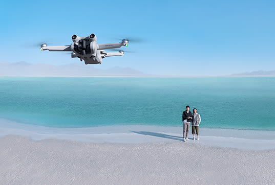 DJI Mini 3 Pro Drohn im Flug mit steuernden Personen im Hintergrund
