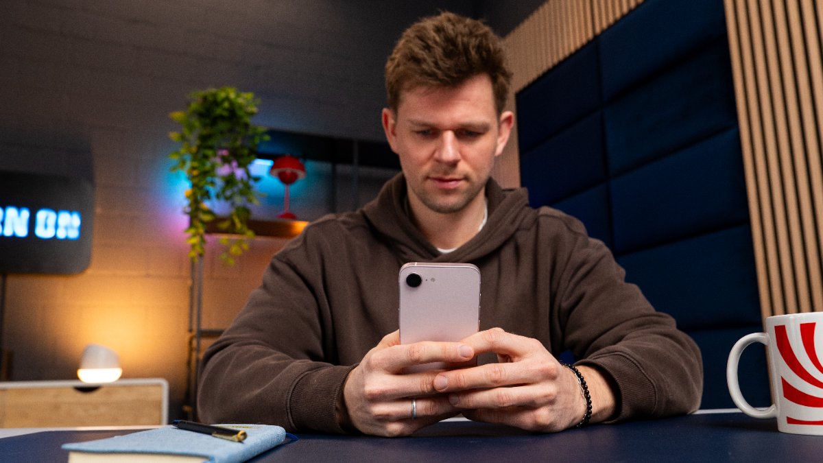 Niklas sitzt an einem Tisch und schaut auf das iPhone 17e, das er in den Händen hält.