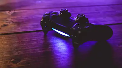Ein schwarzer Gamecontroller liegt auf einem braunen Holztisch, beleuchtet durch blaues Licht.