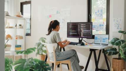Eine Frau programmiert im Home-Office auf einem großen Monitor.