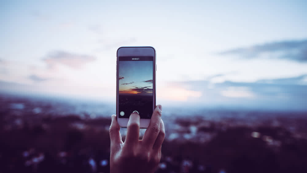 Eine Person filmt mit einem Smartphone den Sonnenuntergang.