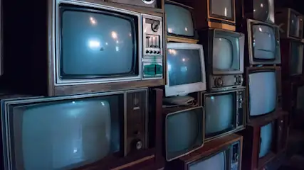 Ein Stapel von alten Fernsehgeräten unterschiedlicher Größe und Farbe, einige mit Knöpfen und Drehreglern.