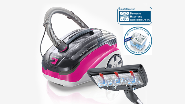 Ein rosa-schwarzer Staubsauger mit Schlauch und Bürste steht vor einem weißen Hintergrund. Zwei Siegel sind im Hintergrund sichtbar.