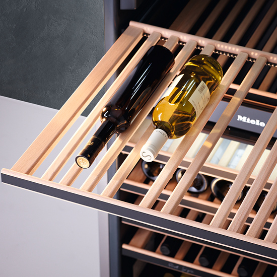 Zwei Weinflaschen liegen auf einem hellbraunen Holzregal im Inneren eines Weinkühlschranks. Das Regal ist teilweise herausgezogen.
