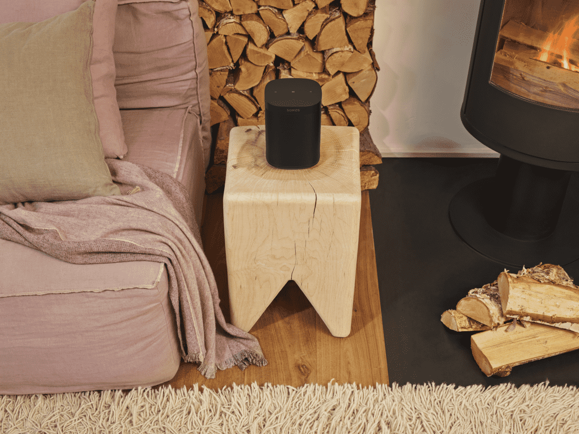 schwarze SONOS One SL auf einem kleinem Holzstand neben einem Sofa