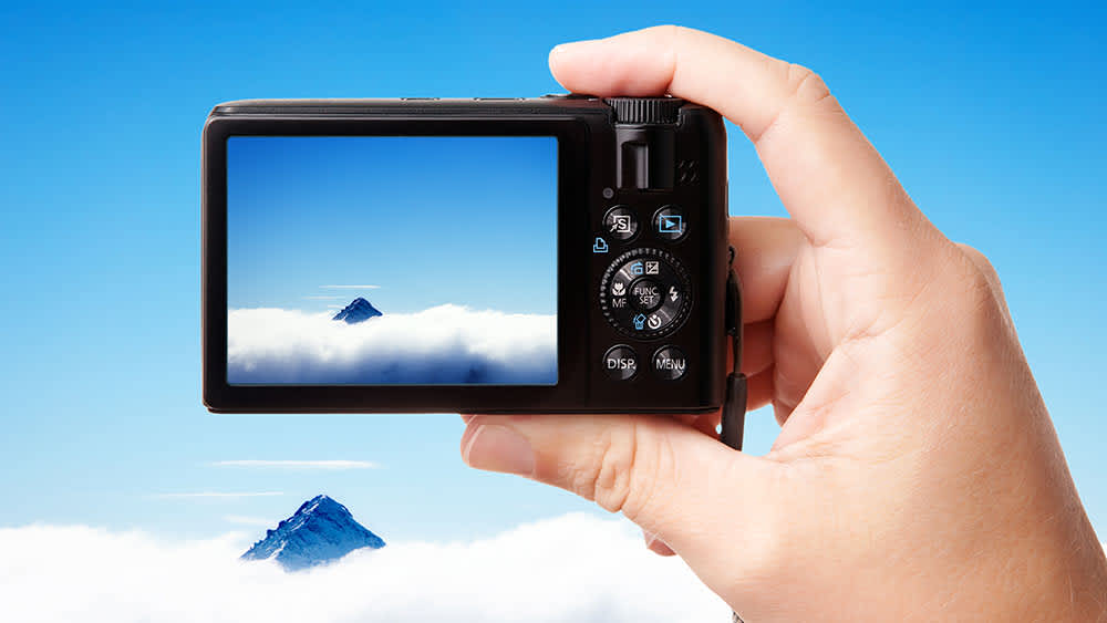 Ein Mann fotografiert mit einer Kompaktkamera den Himmel.