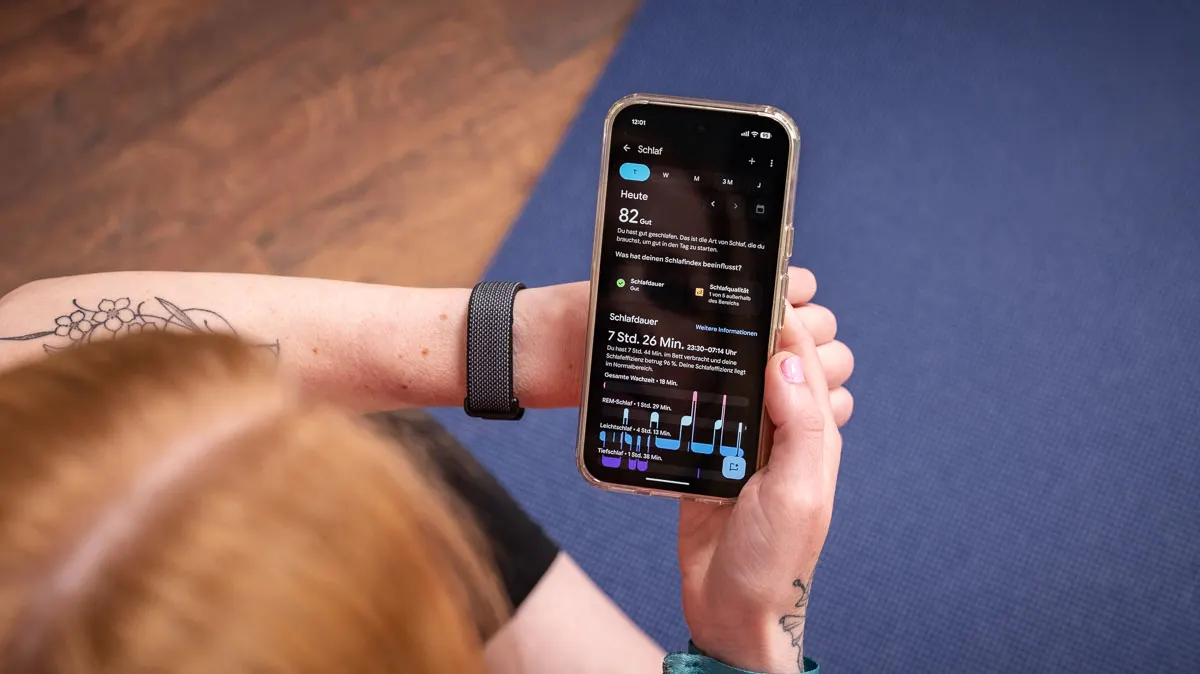 Franzi schaut sich die Schlafanalyse in der Health-App auf dem Smartphone an, am linken Handgelenk trägt sie das Fitbit Air.