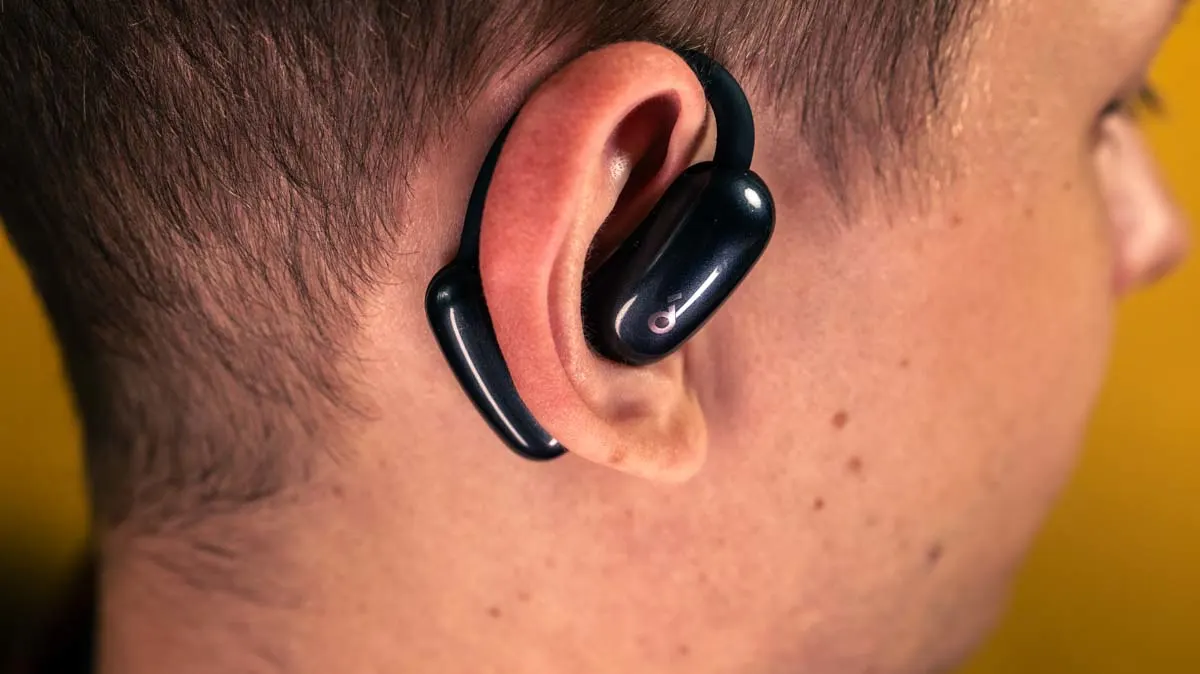 Alex im Profil, wie er einen der Earbuds der Open-Ear-Kopfhörer Soundcore Aerofit 2 mit Ohrbügel über seinem Ohr trägt.