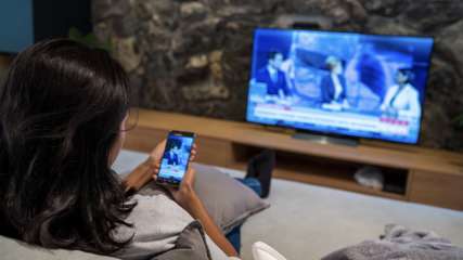 Eine Frau sitzt mit ihrem Handy auf dem Sofa und überträgt Inhalte auf den Fernseher.
