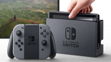 Eine Nintendo-Switch-Konsole in schwarz steht auf einem grauen Tisch vor einem Fernseher.