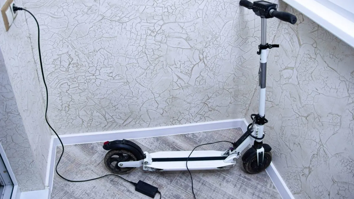 Ein E-Scooter steht mit angeschlossenem Ladegerät in einem kleinen Raum.