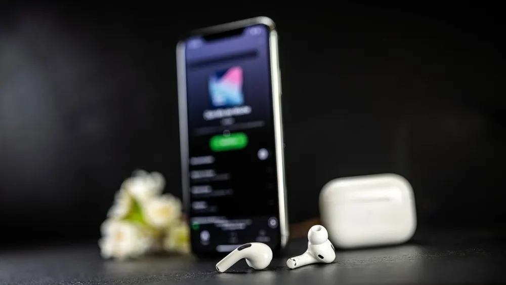 Weiße AirPods liegen vor einem iPhone und einem weißen Ladecase