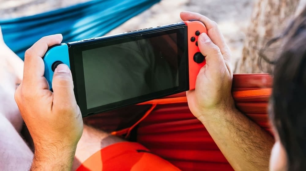 Mann liegt in einer Hängematte und spielt auf der Nintendo Switch