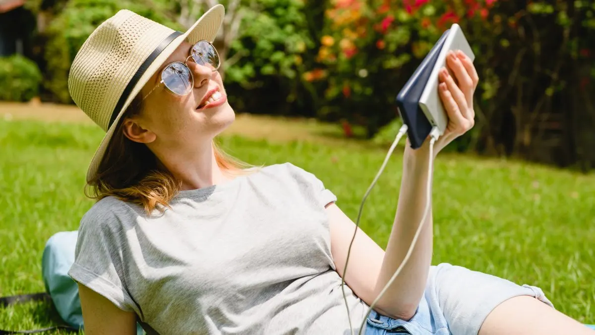 Eine Frau liegt auf einer Wiese mit einem Smartphone und einer Powerbank in der Hand.