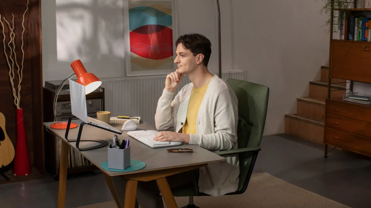Ein Mann sitzt an einem Schreibtisch, seine Hand liegt auf der Logitech-Tastatur Wave Keys.