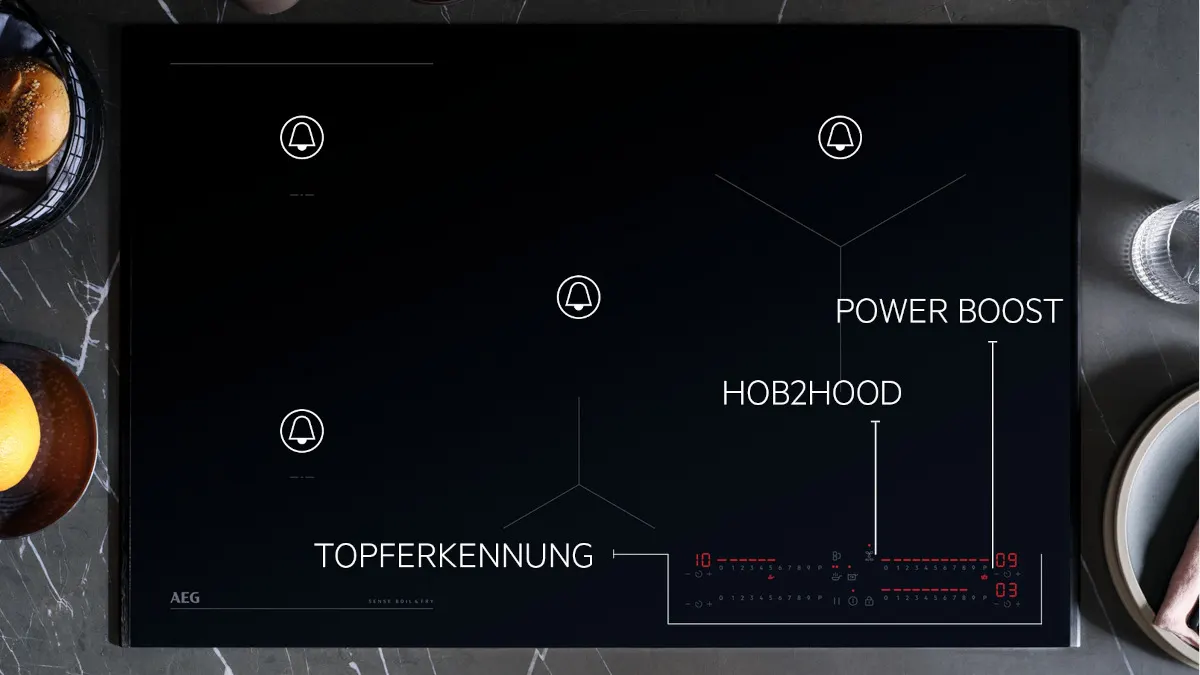 Schwarzer AEG-Induktionsherd mit vier Kochzonen, digitalen Anzeigen und Touch-Bedienelementen auf einer Marmoroberfläche mit Speisen.