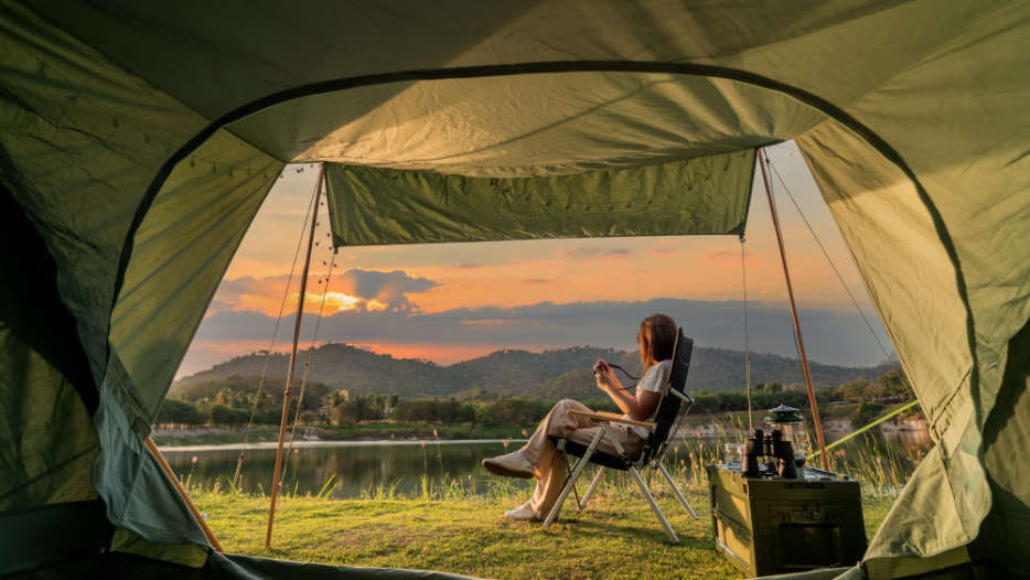 Eine Frau sitzt vor einem Campingzelt bei Sonnenuntergang.