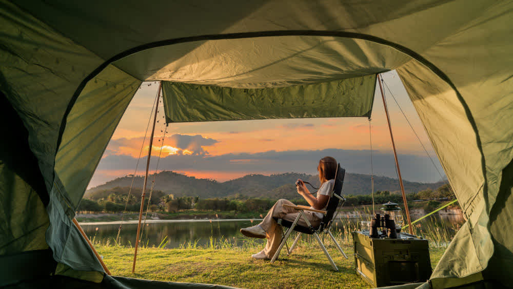 Eine Frau sitzt vor einem Campingzelt mit Sonnenuntergang.