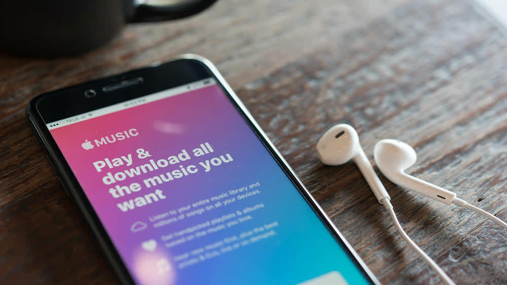 Ein iPhone liegt mit Kopfhörern auf dem Tisch und zeigt Apple Music an.