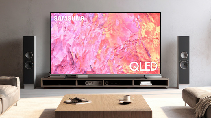 Salon z telewizorem Samsung QLED, głośnikami, sofą i stolikiem kawowym. Na ekranie abstrakcyjny obraz w odcieniach różu.