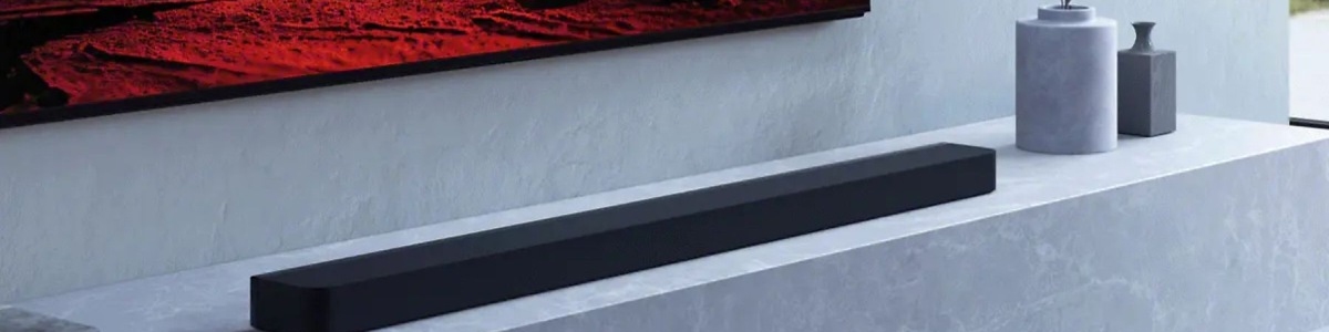 Na ścianie wisi telewizor, pod nim leży czarny soundbar. Obok stoją dwa szare wazony.