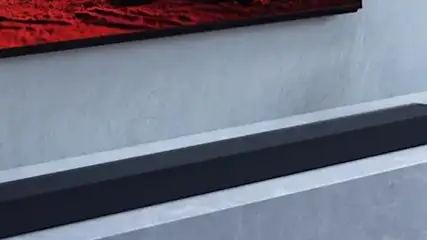 Na ścianie wisi telewizor, pod nim leży czarny soundbar. Obok stoją dwa szare wazony.